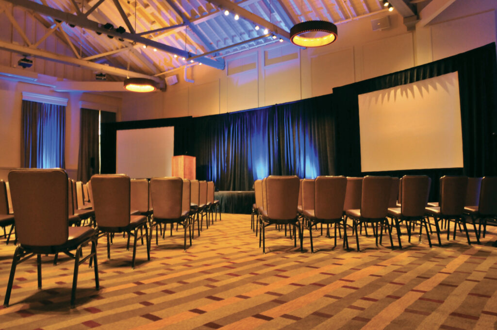 An event space with high ceiling, plenty of chairs and 2 large projector screens 